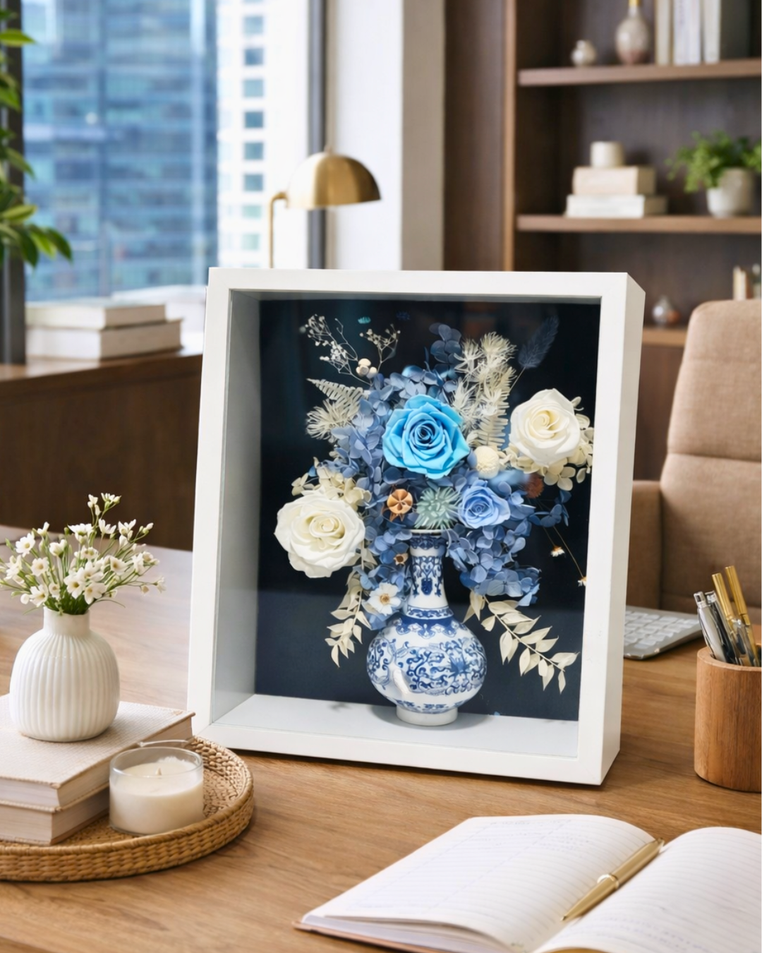 Decorative display of preserved flowers and a vase in a white frame on a table with a cityscape view | Fleur Reverie