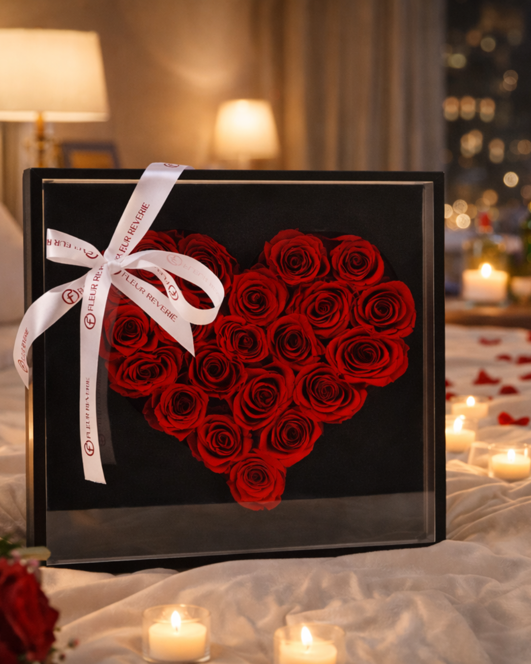 Heart-shaped arrangement of red preserved roses in a black box with a white ribbon, set against a romantic background with candles and soft lighting | Fleur Reverie | Austin TX