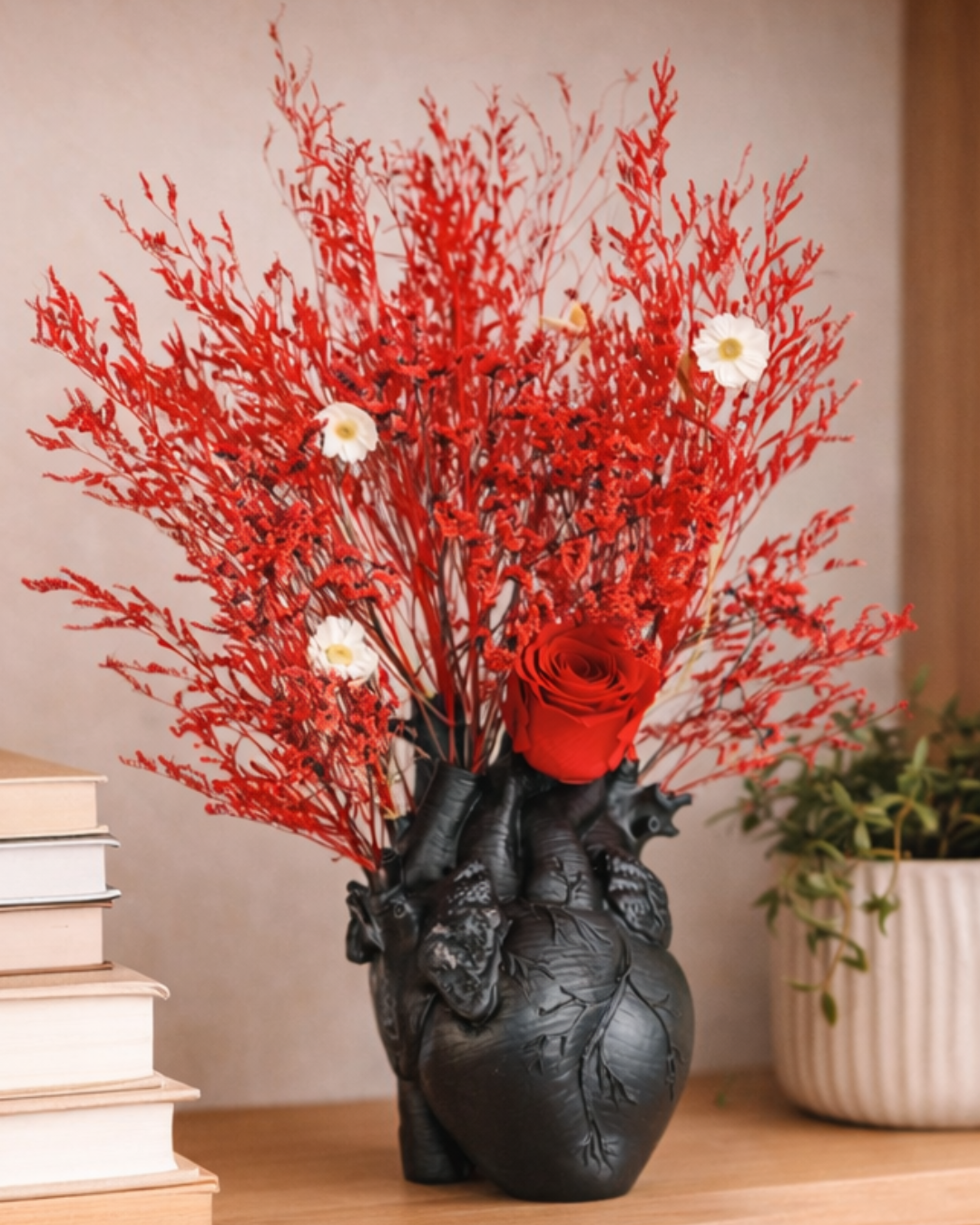 Black heart-shaped vase with red and white preserved floral arrangement on a wooden surface.| Fleur Reverie