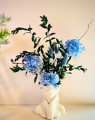 A ceramic lady figural vase with blue preserved hydrangeas and eucalyptus fruits arranged inside it | Fleur Reverie