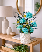 Preserved Floral arrangement in a textured white vase on a wooden table with books and a lamp | Fleur Reverie | Austin TX