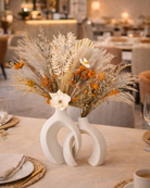 Decorative dried floral arrangement in a white vase on a table in a restaurant setting | Fleur Reverie