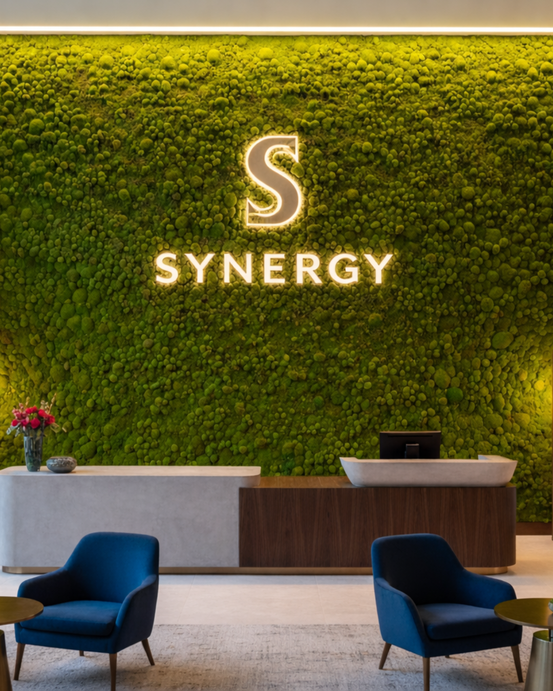 Moss wall with 'SYNERGY' logo and blue chairs in front | Fleur Reverie