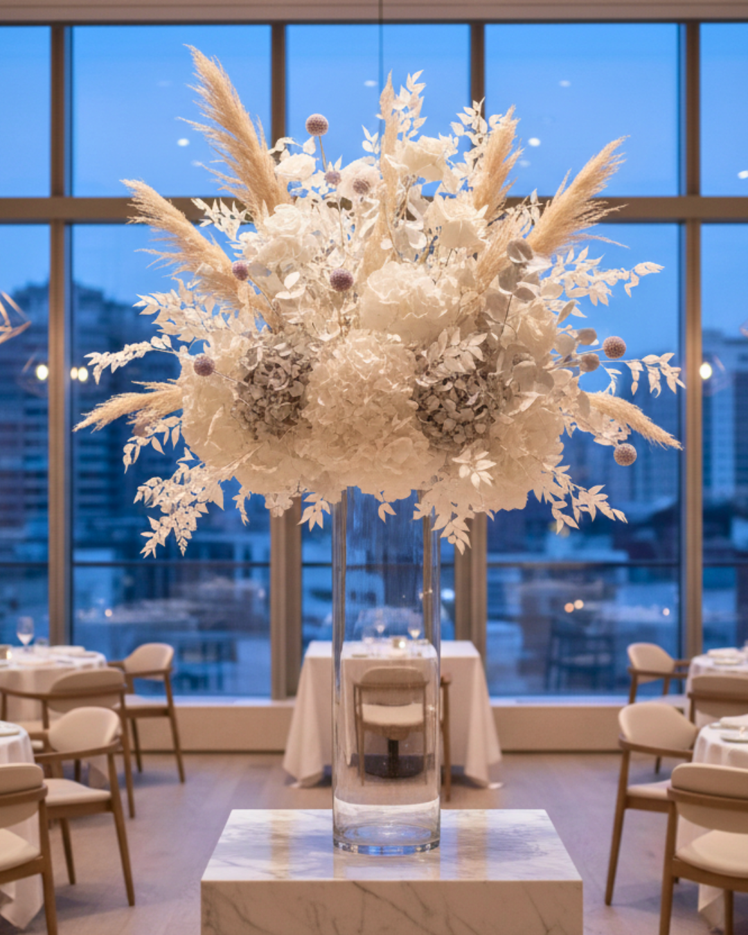 Decorative preserved floral arrangement and dried flowers in a tall clear vase on a table with a cityscape view through large windows | Fleur Reverie | Austin TX