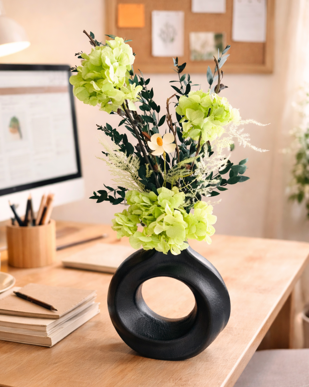 Decorative black vase with green preserved flowers on a desk in an office setting | Fleur Reverie