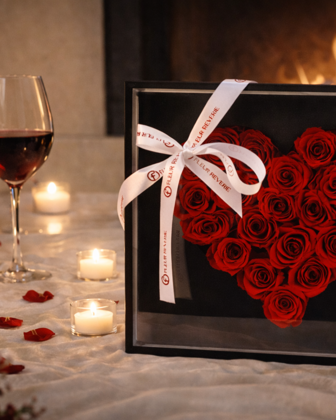 Heart-shaped box of red preserved roses with a white ribbon, wine glass, and candles on a romantic setting | Fleur Reverie | Austin TX