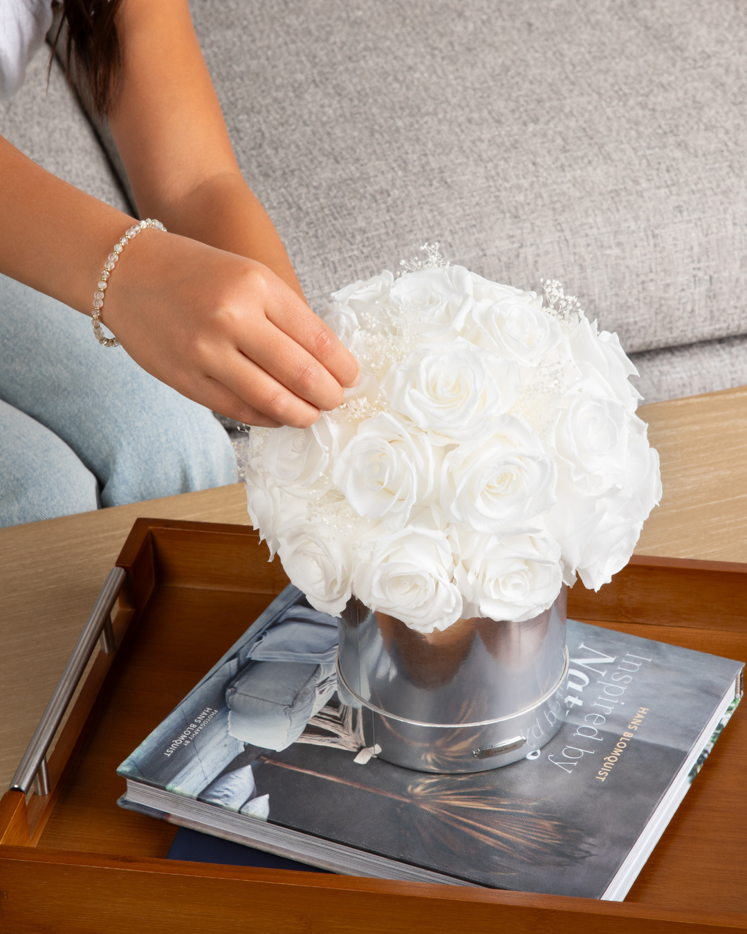 White preserved roses in a vase on a wooden table with a book underneath | Fleur Reverie