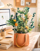 Preserved Floral arrangement in a leather handled handbag on a desk with a computer and books in the background.| Fleur Reverie
