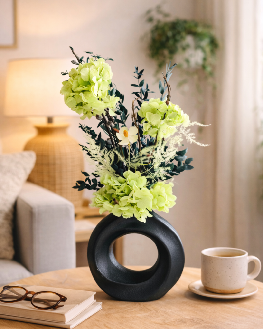 Decorative black vase with green preserved flowers on a table in a living room setting.