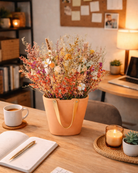 Decorative dried flower arrangement in a peach-colored handbag inspired ceramic vase on a desk with a notebook, pen, and candle | Fleur Reverie