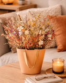 Decorative dried flower arrangement in an orange handbag inspired ceramic vase on a coffee table with a candle and glasses | Fleur Reverie